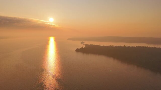 High aerial view captures dense wildfire smoke glowing beneath a dramatic sunrise, with calm water reflecting warm orange light in Nagagamisis Provincial Park.