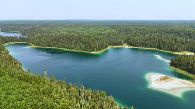 Drone glides above crystal-clear turquoise water bordered by sandy shores and lush forests at Slim Lake in Northern Ontario, Canada.