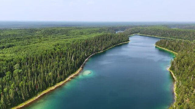 Drone glides above the vibrant blue-green waters of Slim Lake, surrounded by endless forest in the peaceful wilderness of Northern Ontario, Canada.