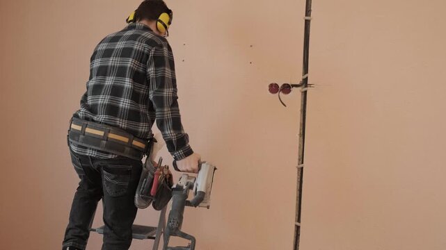 Electrician climbing a ladder with a wall chaser tool preparing for electrical wiring installation and wall cutting during apartment renovation work