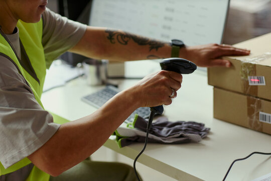Close up of young adult warehouse worker scanning barcode on shipping boxes beside computer, processing orders for fulfillment and inventory use in e commerce logistics marketing