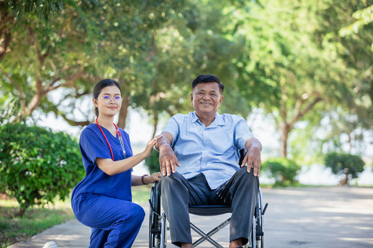 Female nurse cares for elderly man sitting in wheelchair in park. Positive image depicting dedicated professional care for an elderly patient