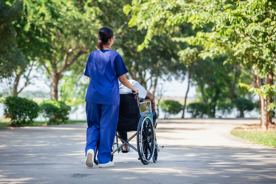 Female nurse cares for elderly man sitting in wheelchair in park. Positive image depicting dedicated professional care for an elderly patient