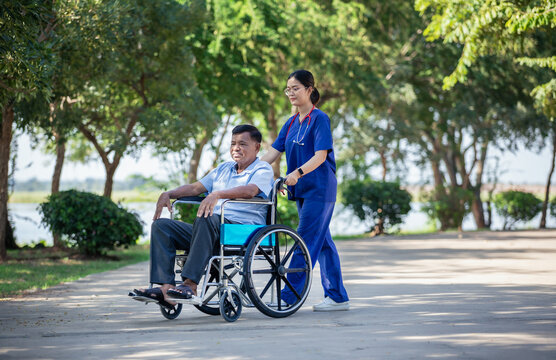 Female nurse pushing elderly man jn wheelchair outdoors serene environment. Image conveys compassionate elderly care and assisted living in a natural setting.
