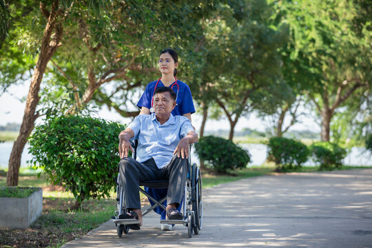 Female nurse cares for elderly man sitting in wheelchair in park. Positive image depicting dedicated professional care for an elderly patient