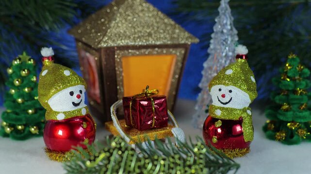 Two snowmen with a gift on a sled and letters against the background of a Christmas lantern and fir trees