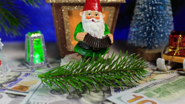 A close-up of a gnome with dollars and a Christmas tree branch among Christmas trees against the backdrop of a Christmas lantern