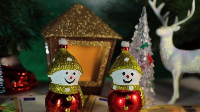 Two snowmen with euro banknotes against the backdrop of a deer with a Christmas tree and a Christmas lantern