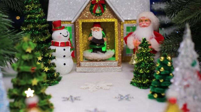 In front of the Christmas house with a gnome on the porch and a snowman with Santa Claus on the sides there are many Christmas trees