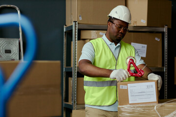 Medium shot of African American young adult warehouse worker sealing shipping box in storage area,...