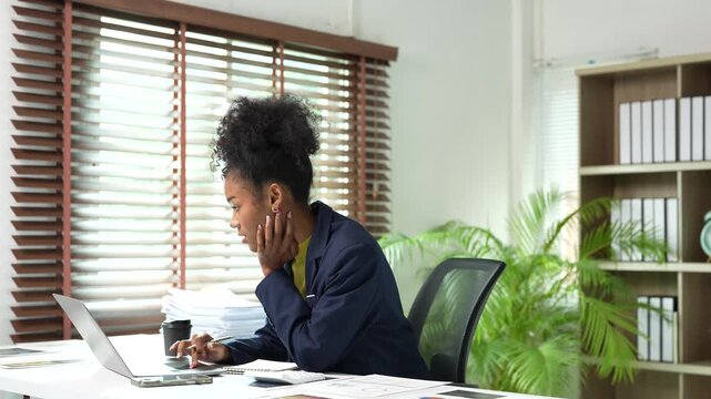 Young african american businesswoman working at her office desk, using a laptop and calculator for financial analysis and taking notes for her startup business project
