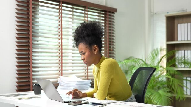 Stressed african american businesswoman typing on laptop computer and analyzing financial reports, feeling tired and overworked while managing corporate business tasks