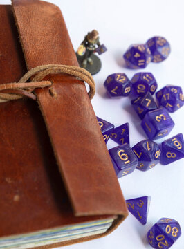 Purple roleplaying dices scattered next to a leather-bound adventure journal, vertical close-up