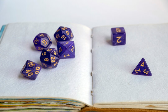 Purple polyhedral dice scattered across the open blank pages of a vintage handmade sketchbook