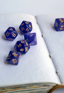 Purple polyhedral dice scattered across the open blank pages of a vintage handmade sketchbook