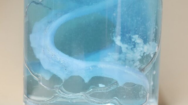 A dental retainer is soaking in water as an effervescent cleaning tablet dissolves. Bubbles form and the water turns cloudy during the cleaning process.