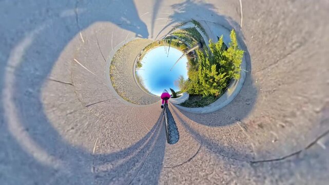 Cycling tiny planet urban park, unique perspective of a person riding a bicycle on a scenic path in sunny weather