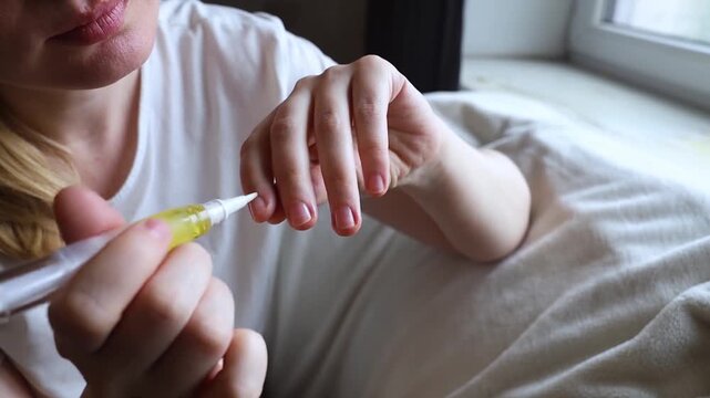 Woman applying nourishing oil on cuticles using a convenient nail cuticle oil pen with brush. Professional home manicure, hand skin health care and treatment.