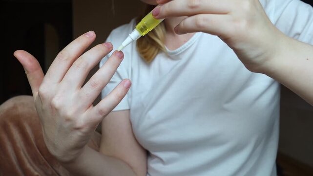 Woman applying nourishing oil on cuticles using a convenient nail cuticle oil pen with brush. Professional home manicure, hand skin health care and treatment.