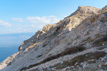 Fototapeta premium A rugged limestone mountain ridge rises above the crystal-blue Adriatic Sea under a clear sky on the Croatian coast