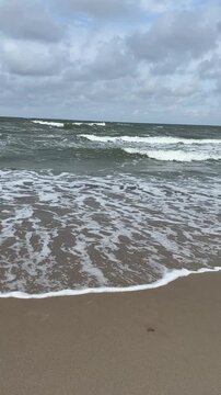 Ocean waves rolling onto sandy beach under cloudy sky  