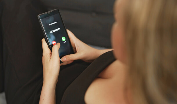 Woman holding smartphone with incoming scam call on screen.