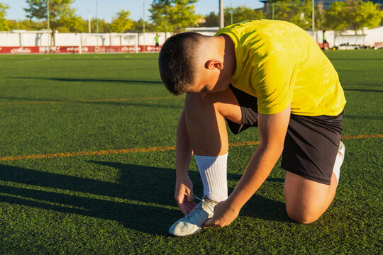 Young soccer player tying cleats on football field