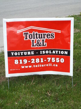 Gatineau,Quebec, Canada &ndash; May 24, 2026: A bright red lawn sign advertises "Toitures L&L" services, specializing in "toiture - isolation" for local residential or commercial roof projects on Chem. d'Ay