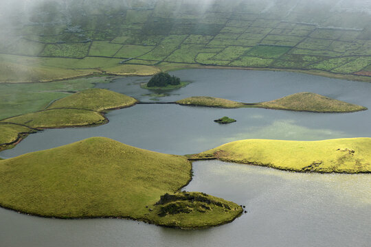 Volcanic crater lake with terraced fields and small islands on a misty day