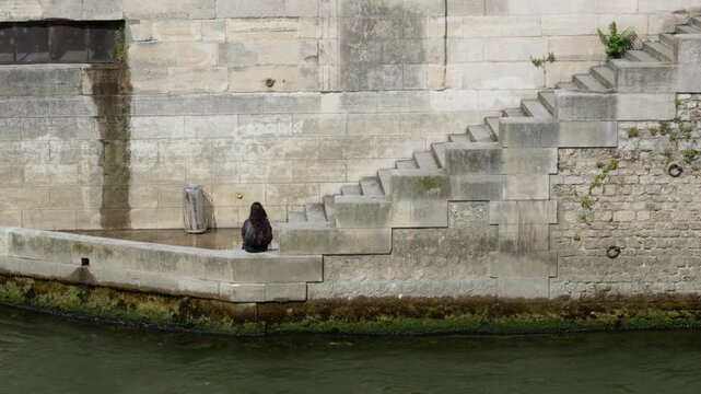Lonely woman sits by stone stairs on urban river bank. This conceptual scene represents mental health depression solitude psychological crisis relaxation and social isolation problems.