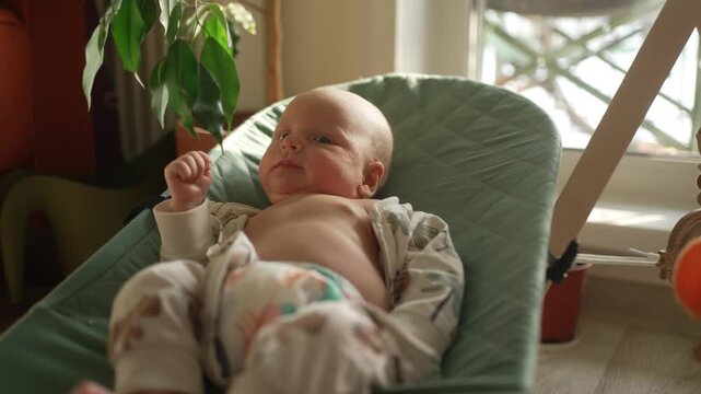 Charming newborn baby lying in a modern bouncer chair, observing the surroundings with curiosity and gentle movements, embodying the beauty of early infancy and new beginnings