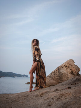Fashion model wearing abstract print beach kimono posing on rocky tropical shoreline by calm ocean