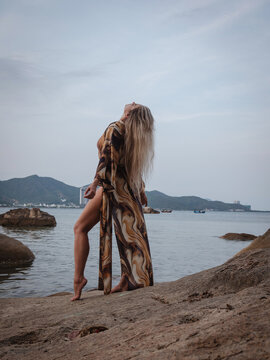 Woman in flowing abstract print beach kimono enjoying peaceful moment on rocky tropical shoreline