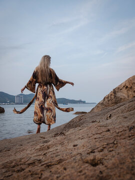 Woman in flowing abstract print beach kimono enjoying peaceful moment on rocky tropical shoreline