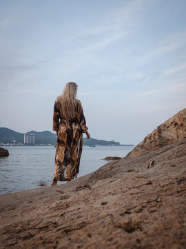 Woman in flowing abstract print beach kimono enjoying peaceful moment on rocky tropical shoreline