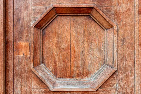 Detailed close up view of an octagonal geometric wood panel on a vintage brown wooden door exterior