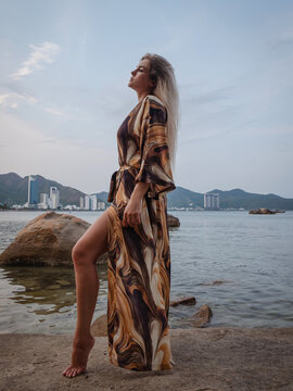 Fashion model wearing abstract print beach kimono posing on rocky tropical shoreline by calm ocean
