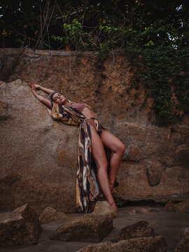Woman in flowing abstract print beach kimono posing against natural coastal rock formation