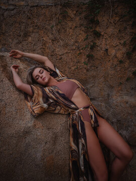 Woman in flowing abstract print beach kimono posing against natural coastal rock formation