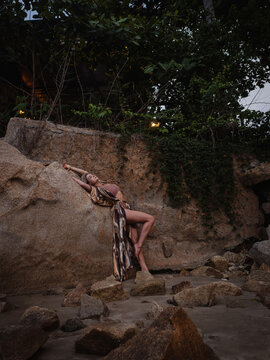 Woman in flowing abstract print beach kimono posing against natural coastal rock formation
