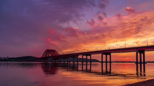 Twilight timelapse of Banghwa Bridge over the Han River, scenic architectural silhouette under a dramatic pink sunset sky with perfect water reflection in Seoul, South Korea.