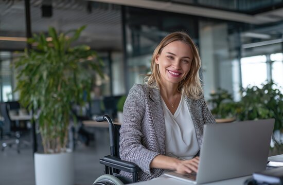 A mature chic female worker in a patterned blazer uses a laptop in a bright contemporary office interior next to an indoor plant. Concept of eco-friendly and inclusive workspace.
