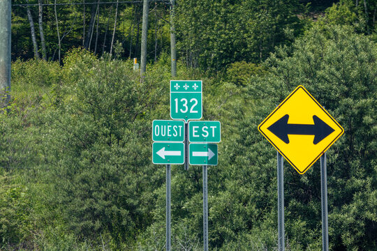 Quebec, Canada, 29 June 2026 : Green road signs for Route  and directional arrows for West and East stand with a yellow warning sign.