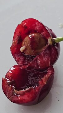 White worms crawl together into the core of ripe red cherry with juicy pulp, close-up, macro. Nutrition of cherry fly larvae. Spoiled, poor quality berry crop. 