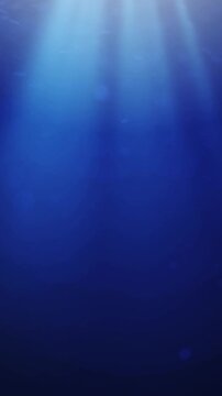 Sunlight beams through deep blue ocean water with floating particles