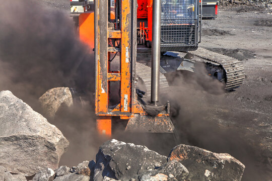 Mining equipment blasting rocks in a coal mine, with black clouds of coal dust erupting. 