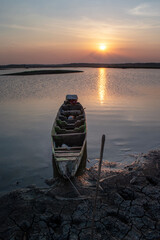 Obraz premium A fisherman's boat rests at the lake's edge at sunset, a small wooden boat on the dry lakeshore.