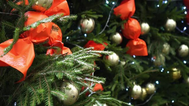 Christmas tree outdoors adorned with vibrant baubles, ribbons, and lights. The evergreen branches hold red and gold ornaments, enhancing the festive holiday ambiance.