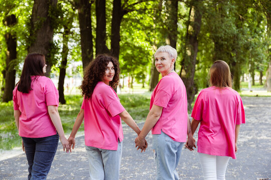 Women wearing pink t shirts walking holding hands in park