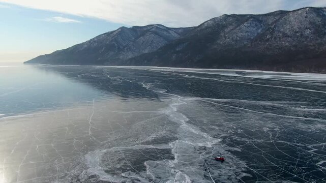 Peaceful Portrayal Of Single Red hovercraft Traveling Across Icy Lake Surface To Mountainous Edge
